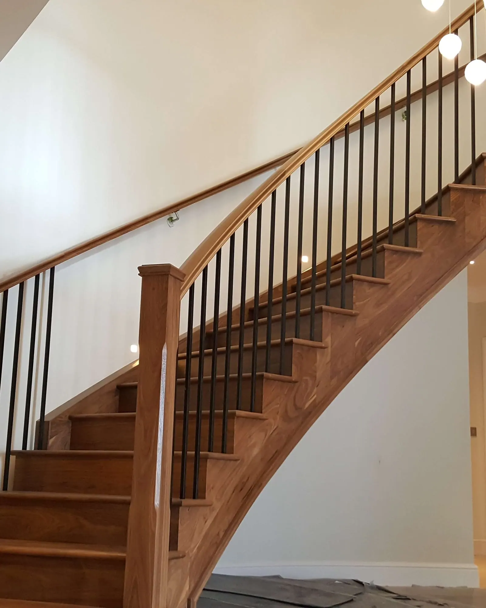 Curved walnut staircase with black metal spindles rising to a pendant-lit landing