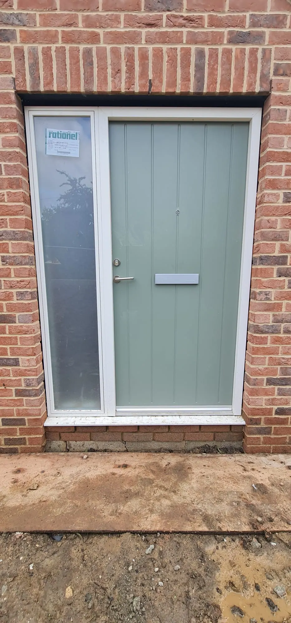 Sage green composite front door with a glazed side panel in a brick opening