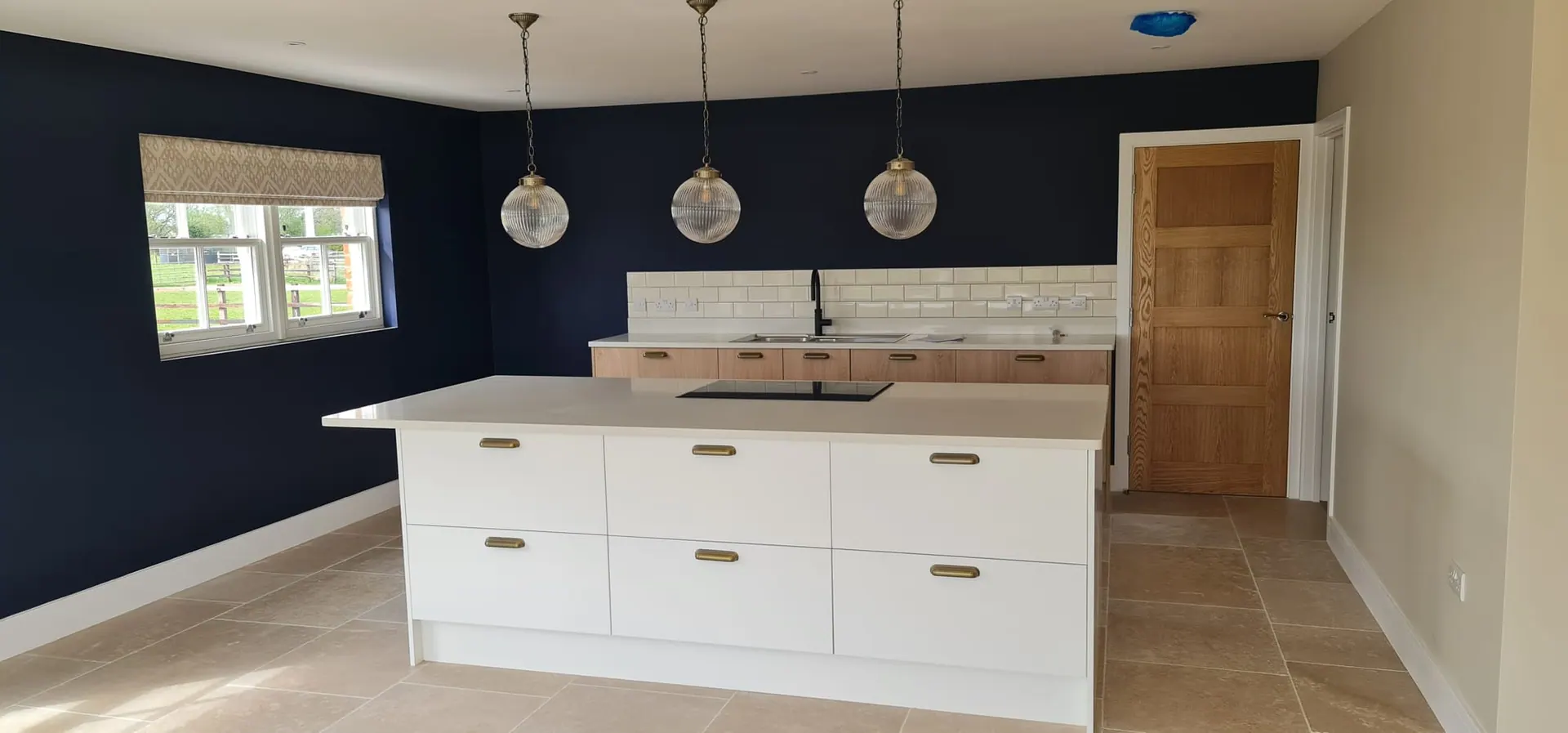 White kitchen island under glass pendants against a navy wall