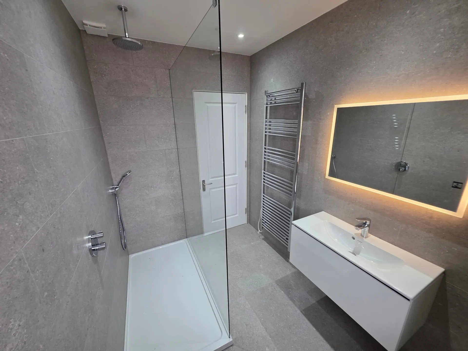 Wetroom with a frameless glass screen, wall-hung vanity and lit mirror